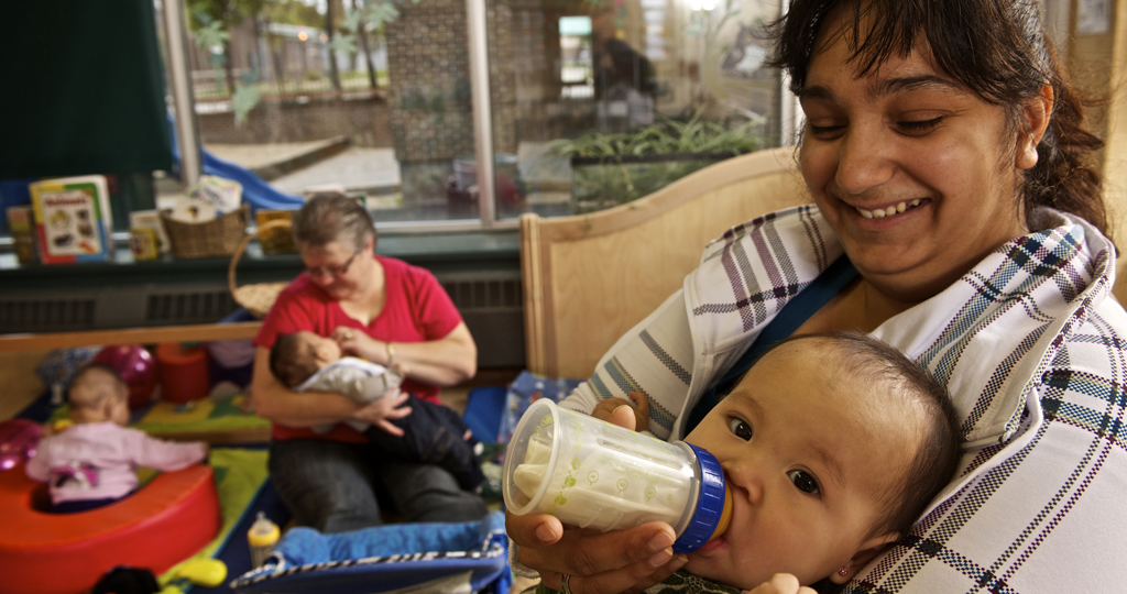 Early childhood educator sitting in a rocking chair bottle feeding an infant